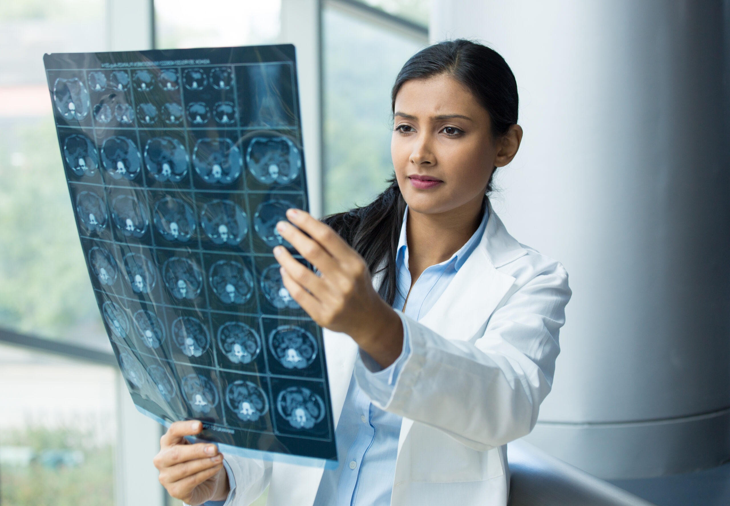 Closeup portrait of intellectual woman healthcare personnel with white labcoat looking at full body x-ray radiographic image ct scan mri isolated hospital clinic background. Radiology department